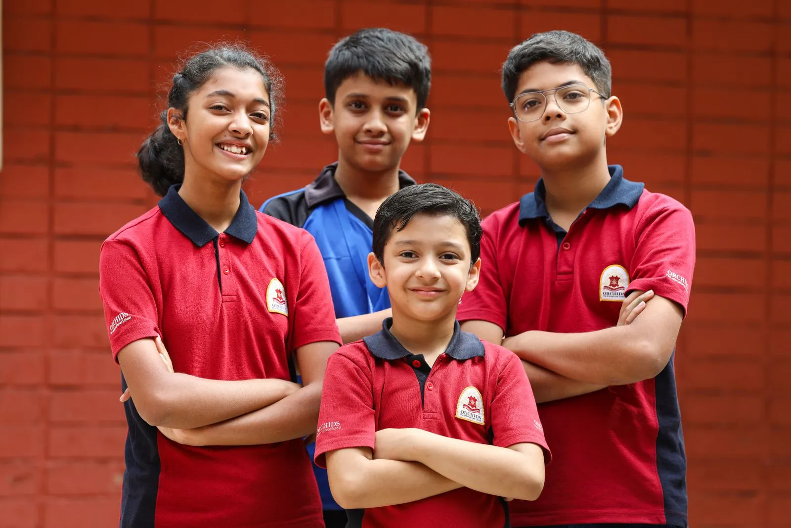 Four students in red house shirts standing together in front of a brick wall