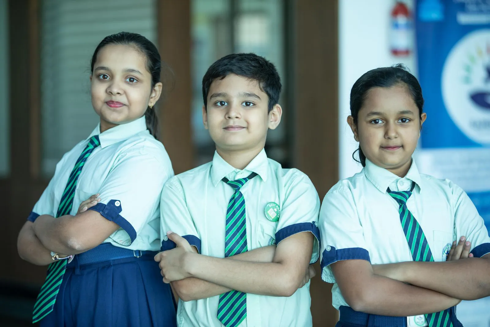 Three middle school students in white and green uniforms standing with arms folded
