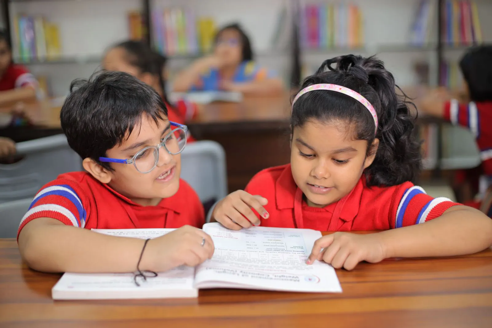 Two primary students reading one book together at a desk